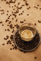 Hot espresso with foam in glass cup on vintage plate with aromatic roasted coffee beans on wooden table. Copy space. Alternative Coffee brewing concept.