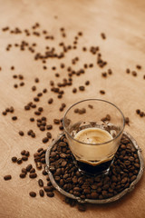 Hot espresso with foam in glass cup on vintage plate with aromatic roasted coffee beans on wooden table. Copy space. Alternative Coffee brewing concept.