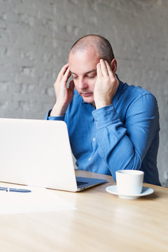 A man suffers a headache, sits at work in the office at a laptop, rubs his hands with whiskey. The concept of overwork, stress, processing
