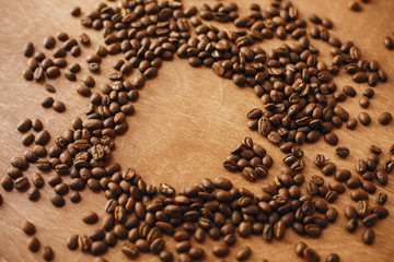 Coffee cup shape made in roasted coffee beans on wooden table. International coffee day. Coffee shop or cafe concept. Creative idea. Coffee mug and beans