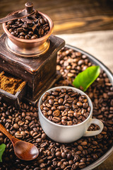 Fototapeta premium Wooden vintage hand coffee grinder and mug on a pile of brown coffee beans. Grinding fragrant freshly roasted coffee