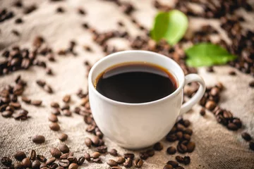 Gordijnen A mug of strong black coffee and scattered grains. Fragrant invigorating drink from freshly roasted coffee beans © Artem
