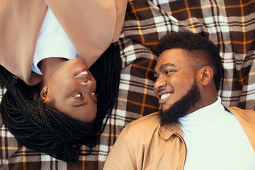 Top view of romantic afro couple lying on picnic plaid outdoors