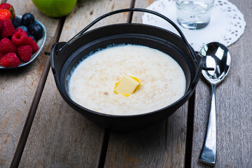 Traditional breakfast milk porridge with butter and berries on a wooden table.