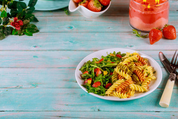 Tricolor rotini pasta from durum wheat with green salad on wooden table.