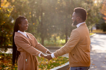 Black romantic couple holding hands while having date in autumn park