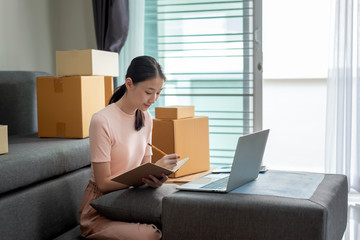 Asian woman student and small businesses online working at home taking note the customer order.