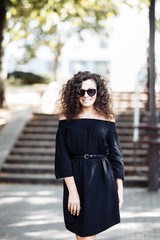 Fototapeta premium Portrait of a curly young brunette woman in sunglasses on a sunny summer day.