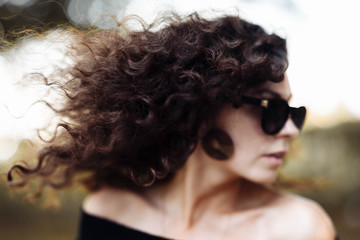 Portrait of a curly young brunette woman in sunglasses on a sunny summer day.