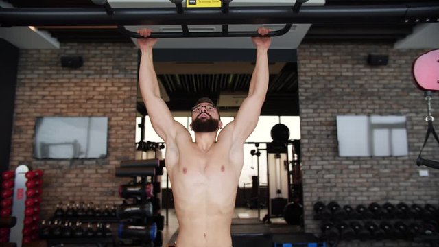 Ripped Shirtless Man Doing Pull-Ups in the Hardcore Gym.