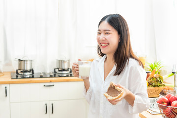 Obraz na płótnie Canvas Happy young girl eating bread with a glass of milk for breakfast in kitchen. Healthy eating and lifestyle concept.