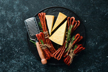 Smoked sausages with cheese on a black stone background. Parmesan, Kabanosy. Top view. Free space for your text.