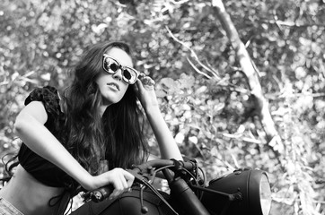 Fototapeta na wymiar young sexy woman with long wavy hair in leather clothes and sunglasses posing near a motorcycle. Black and white photo.
