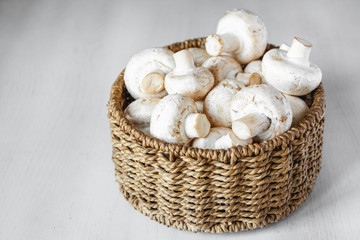 Fototapeta na wymiar Mushrooms champignons in a round wicker basket on a white wooden table. Place for text or advertising