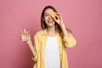Young woman with glass of lemon water on pink background