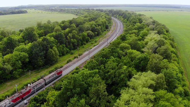 Aerial shot of freight train that travels by rail. Train carries goods and raw materials for heavy industry. Railways are surrounded by trees and endless green fields. Taken by drone at sunset