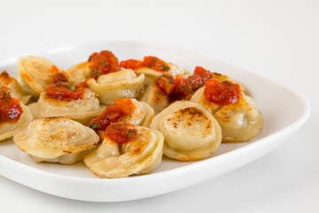 Russian food pelmeni, fried meat dumplings on white plate, with tomato sauce, isolated