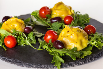 Steamed meat dumplings Manti with tomatoes, black olives, and greens on black stone plate. Dough made with addition of curcuma for yellow color.