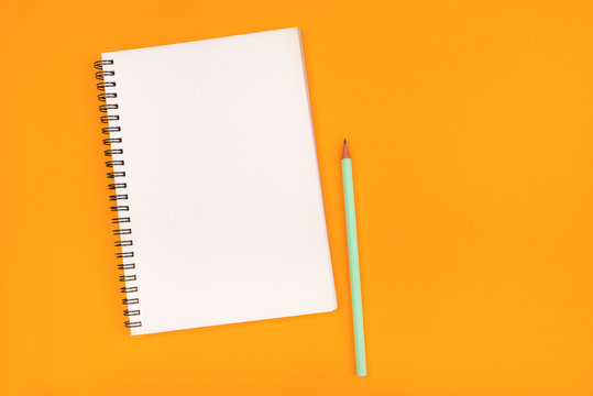 Empty notebook and pencil on orange background, top view. Copy space.