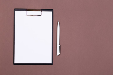 Clipboard with a white sheet and pen on a gray-dark background. View from above. space for text