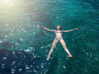 Young slender European girl in swimsuit swimming in clear blue transparent sea water. She enjoying her summer holidays.
