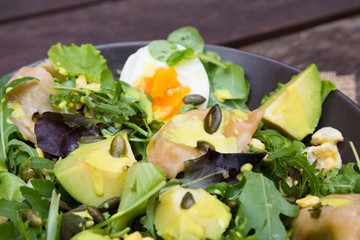 Salad with avocado, dumplings, eggs, pumpkin seeds, arugula and other greens on wooden table in the village. Healthy food concept.