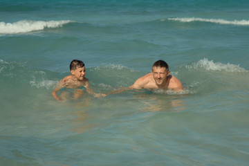 European man and his son are swimming in the ocean together during their vacations. Healthy lifestyle.