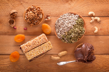 Bars of sports nutrition from nuts, seeds and chocolate paste - vegetable natural protein, a mixture of dried fruits, assorted nuts and seeds on a wooden table. Top view