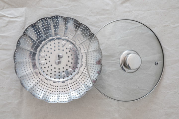 Steel steamer insert for healty cooking, with pan cover, on grey paper, top view