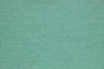 The textile surface is turquoise or aquamarine. Book cover. View from above. Not new, with spots and scuffs. Background or wallpaper. Reduced contrast. Macro