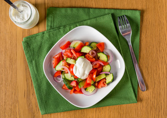 Fresh salad with tomato, cucumber and onion, seasoned with sour cream. Placed on wooden table with green placemat. Top view, flat lay.
