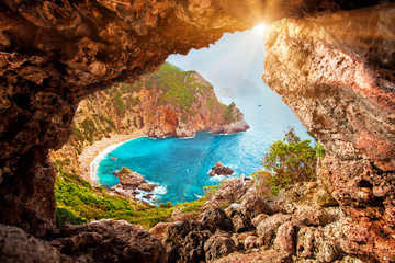 Beautiful magical view of the Gyali beach in Corfu, Greece through a hole in the rock at sunny day. amazing places. popular tourist atraction. - obrazy, fototapety, plakaty