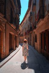 Rear view of a young woman walking in a narrow and old street of Solsona, Spain. Teal and orange