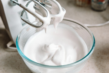Baking concept. Whipped cream of egg whites for perfect peaks in a glass bowl, with a mixer on a...