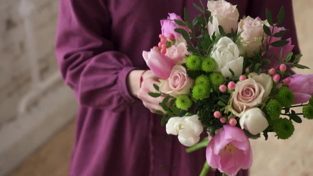 Woman florist makes bouquet of flowers in workshop, close up of hands