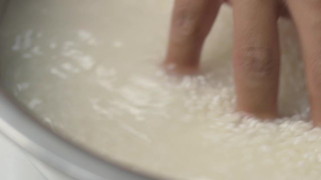 Making Japanese sushi rice, close up hand washing rice in metal bowl.