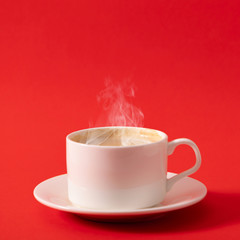 Steaming coffee cup on red background. White сoffee cup with steam. Front view, copy space