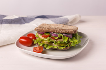 Homemade sandwich with ham, tomato, cucumber and onion on a white plate and white background, horizontal orientation.