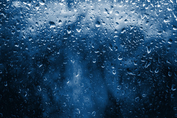 Classic blue toned Spring Rain drops on window and tree in background