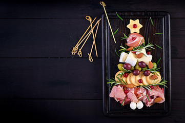 Antipasto platter with ham, prosciutto, salami, cheese,  crackers and olives on a wooden background.  Christmas table. Top view, overhead