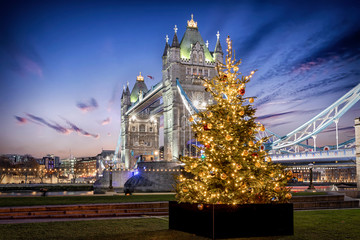 Die Tower Bridge in London bei Nacht mit einem festlich beleuchtetem Weihnachtsbaum davor,...