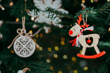 Wooden deer Christmas decoration toy on Christmas fir tree with garland lights bokeh. Traditional new year symbol