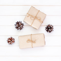 Christmas gifts in craft packaging with pine cones on white wooden background. Festive composition, square