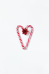 Christmas composition, heart made of two caramel candy canes and red bow on white background. Festive minimal style flat lay. For greeting card, invitation, social media. Vertical orientation