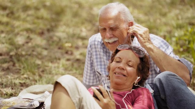 Old people, senior couple, elderly man and woman, husband and wife in park, retired seniors. Outdoors activity, leisure, fun, recreation. Grandpa and grandma listening to song, music with mp3 player&nbsp;