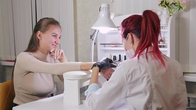 Woman manicurist with gloves in a beauty salon does a hardware manicure to a client before applying a gel coating