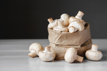 Mushrooms champignons in paper bag on a white wooden table. Close up. Place for text or advertising