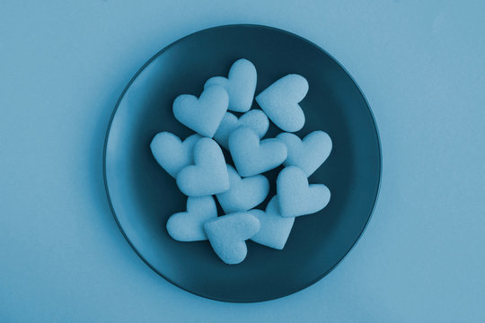 Blue hearts shaped cookies on the dark plate in the center of the blue background. Top view. Copy space. Creative food collage.