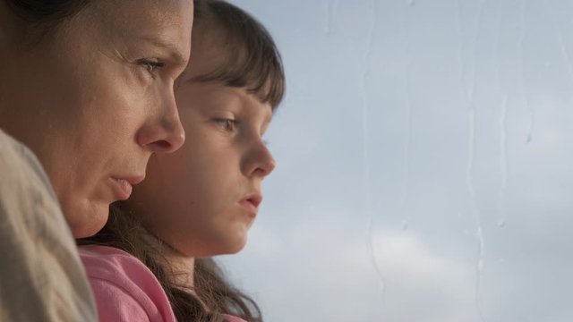 Woman with a child are sad at the window. Portrait of mother and daughter looking out the window. Quarantine concept.