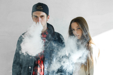 Vaping teenager. Young cute girl in casual clothes and handsome guy in a cap smoke an electronic cigarette outdoors. Bad habit that is harmful to health. Vape activity.
